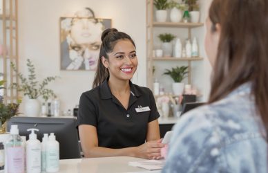 Receptionist at a beauty salon welcoming a client with a smile — ideal for showcasing front office roles in the beauty and wellness industry.
